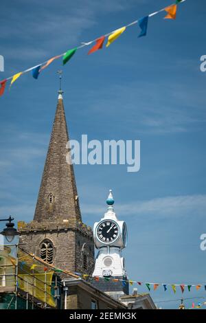 La guglia della chiesa di St Thomas Dodbrooke e St Edmund, e l'orologio sul Kings Cinema, Fore Street, Kingsbridge, Devon, Regno Unito. Foto Stock