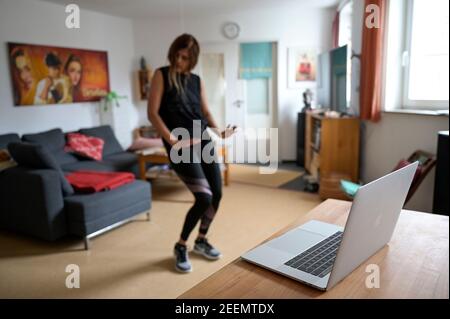 GERMANIA, Amburgo, corona pandemia, giovane donna che fa sport a casa con streaming online di club sportivo, Apple macbook schermo con Zumba sessione di danza Foto Stock