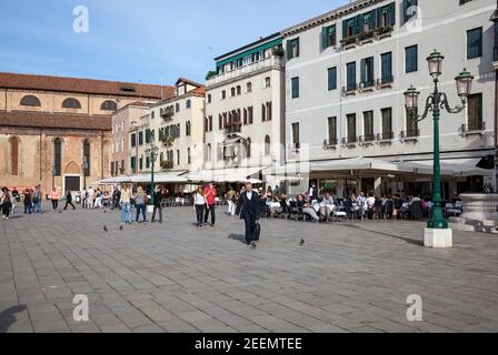 Le persone si rilassano e si godono il sole sotto un cielo blu limpido presso i caffè pavement su campo Santo Stefano a Venezia, Italia con spazio per le copie Foto Stock