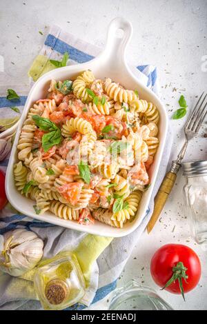 Dieta primaverile pasta vegana sana. Fusilli italiani con pomodori, verdure verdi, erbe fresche, formaggio cremoso o feta, su sfondo bianco c Foto Stock