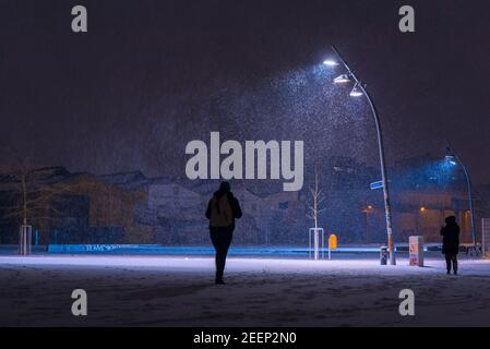 La neve si flurries su una piazza la sera, luci di strada e fiocchi di neve, nevica la sera su una grande piazza illuminata, una persona Foto Stock