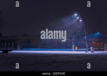 La neve si flurries su una piazza la sera, luci di strada e fiocchi di neve, nevica la sera su una grande piazza illuminata Foto Stock