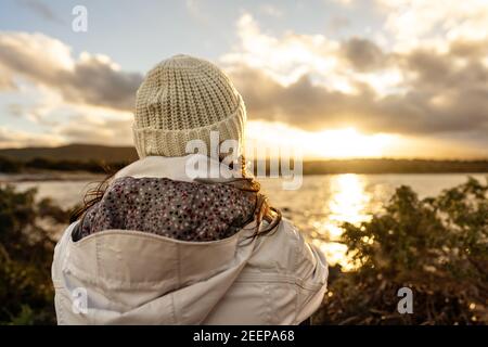 Vista personale pensiva dal retro guardando l'orizzonte. Donna irriconoscibile visto da dietro vestito in lana d'inverno con cappuccio vestiti guarda a uno meraviglioso Foto Stock