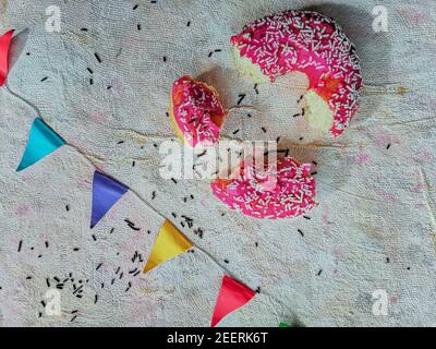 Posa piatta di frammenti di ciambella rosa con triangoli colorati su sfondo tessuto leggero Foto Stock