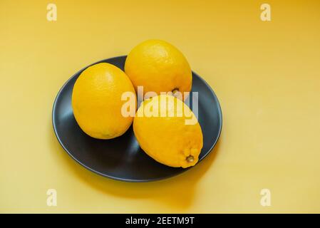 Tre limoni su un piatto nero su sfondo giallo. Sfondo. Agrumi, frutta Foto Stock