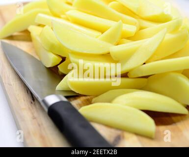Un mucchio di patate crude tagliate a fette sul piatto di legno con il coltello dello chef. Foto Stock