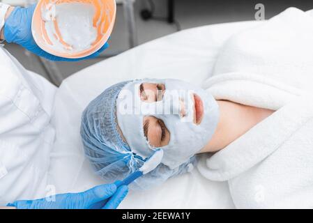 Una ragazza in un abito bianco ottiene una maschera di alginato sulla sua faccia. Foto Stock