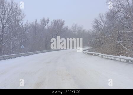 Strada coperta di neve senza auto. Alberi in brina sul lato della strada. Nevi bianche in inverno. Maltempo concetto per i conducenti. Foto Stock
