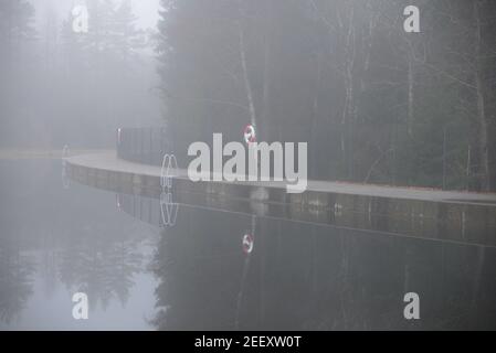 Lago con una diga in un giorno di autunno nebbia Foto Stock