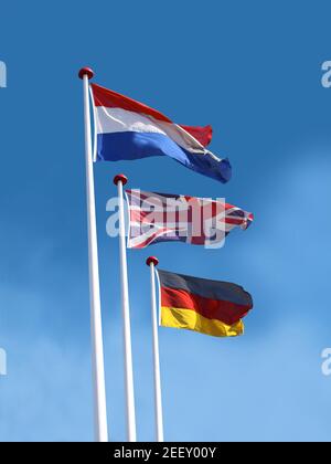 Bandiere di Francia, Regno Unito, Germania su pali di bandiera. Bandiera della Francia è in cima. Sfondo blu cielo. Foto Stock