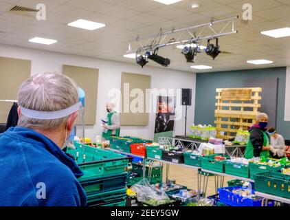 Un uomo anziano che indossa una maschera facciale e uno scudo facciale presso una foodbank Trussell Trust dove le donazioni alimentari vengono erogate a coloro che vivono in povertà alimentare. Foto Stock