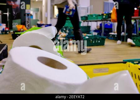 Una foodbank Trussell Trust a Colindale, Londra, con rotolo di carta igienico in primo piano e persone e volontari che raccolgono donazioni di cibo in background Foto Stock