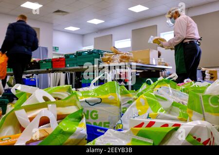 Una foodbank Trussell Trust a Colindale, Londra, con borse piene di cibo in primo piano e persone e volontari che raccolgono donazioni di cibo in background Foto Stock