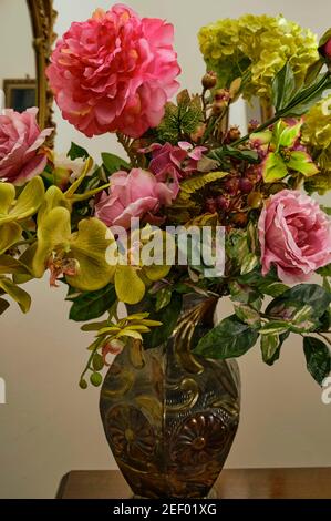 Una colorata disposizione di fiori artificiali in fiore in un vaso di metallo multicolore. Foto Stock