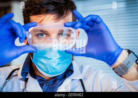 medico che mette su googles protettivi Foto Stock