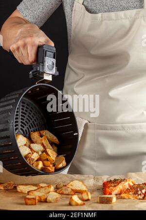 Una donna caucasica cuoca sta scaricando la patata fritta appena fatta trita su un pezzo di carta da forno che ha tre filetto di salmone marinato arrosto al forno con Foto Stock