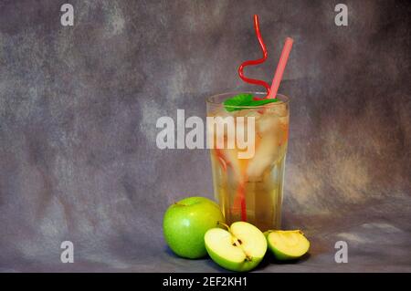 Mele verdi mature e un bicchiere di succo di frutta con ghiaccio su sfondo grigio. Primo piano. Foto Stock