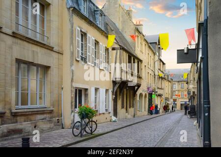 Pittoresca strada francese nella città di Bayeux Francia in Normandia con una bicicletta parcheggiata contro una colorata scatola di fiori e gli amanti dello shopping. Foto Stock