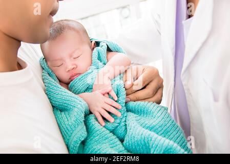 Medico che mette delicatamente il neonato addormentato nelle braccia del padre Foto Stock