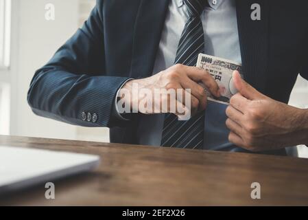 Uomo d'affari che mette i soldi, le banconote giapponesi dello yen, nella sua tasca del vestito - concetto di corruzione Foto Stock