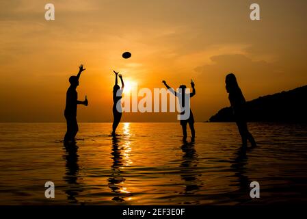 Silhouette di persone che giocano in spiaggia al tramonto estivo Foto Stock