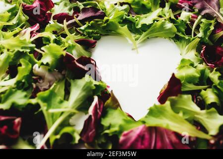 Forma del cuore da foglie di insalata verde e viola mescolano lo sfondo. Tavola bianca. Foto di alta qualità Foto Stock