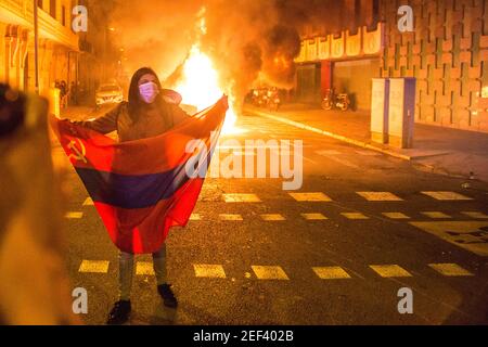 Un manifestante detiene una bandiera comunista di fronte a un contenitore di rifiuti in fiamme durante la dimostrazione.Pablo Hasél, un rapper catalano, è stato arrestato il martedì mattina, febbraio 16 ed è stato condannato a nove mesi e un giorno di prigione dalla Camera d'appello della Corte Nazionale nel settembre 2018, oltre al pagamento di una multa di circa 30,000 euro accusati di glorificare il terrorismo, insultare e calunniare la monarchia e le forze di sicurezza dello stato. Nel pomeriggio dello stesso giorno, a Barcellona, centinaia di persone hanno protestato contro il suo arresto, la manifestazione si è conclusa con i conflitti Foto Stock