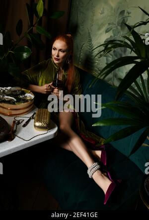 Splendido vamp donna dai capelli rossi ricco ha un buon tempo in ristorante di pesce mangiare ostriche, bere vino Foto Stock
