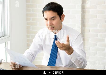 Uomo d'affari asiatico sempre sconvolto e deluso dopo aver letto il documento a. la sua scrivania Foto Stock