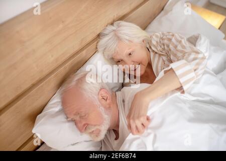Donna anziana dai capelli grigi che abbracciava il marito addormentato Foto Stock