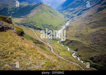 Maestose montagne del Caucaso con una splendida vista. Vegetazione verde e arbusti su pianure lisce. Il fiume scorre lungo la strada. Magnifico Foto Stock