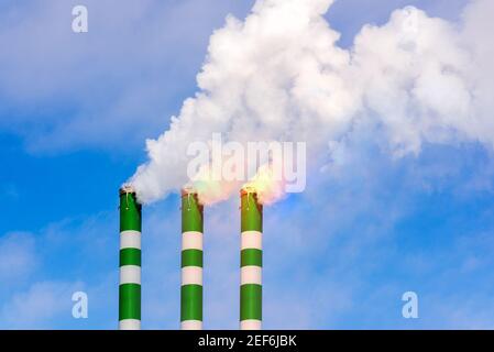 Tre tubi industriali di fumo da camino su cielo blu nuvoloso.il fumo bianco emana dai tubi. Foto Stock