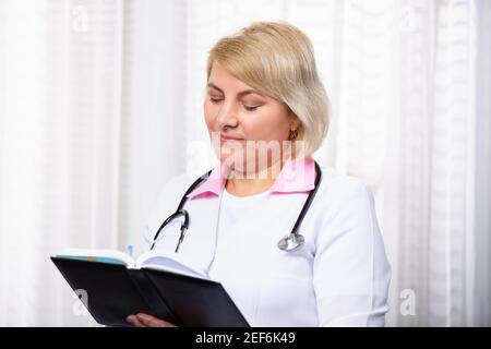 Note mediche professionali su riviste mediche. Donna medico o farmacista in bianco cappotto di scrittura in taccuino di carta. Messo a fuoco serio vecchio di mezza età Foto Stock