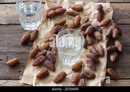 Datteri essiccati frutta su un ramo e un bicchiere d'acqua su un tavolo di legno. Tradizionale fast breaking, pasto serale musulmano durante il santo Ramadan Foto Stock