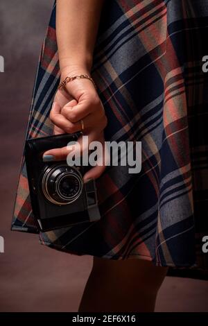 Mano della ragazza che tiene una macchina fotografica vicino all'orlo dell'abito, cornice verticale, fotografia da studio su uno sfondo grigio Foto Stock