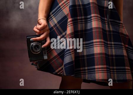 Mano della ragazza che tiene una macchina fotografica sull'orlo dell'abito, fotografia da studio su uno sfondo grigio Foto Stock