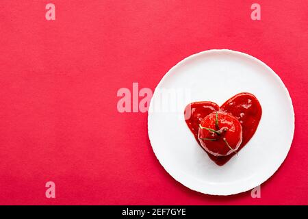 Pomodoro a forma di cuore in pasta di pomodori, su un piatto bianco. Moderna e creativa natura morta. Foto Stock