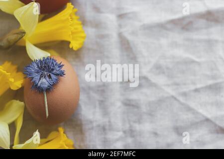 Buona Pasqua! Uovo di Pasqua elegante decorato con fiori blu secco su tovagliolo rustico di lino con narcisi gialli, piatto. Spazio per il testo. Natu creativo Foto Stock