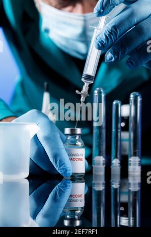 Medico con tappi medici e guanti in lattice raccoglie il vaccino covid con una siringa in un tavolo con diversi fiale Foto Stock