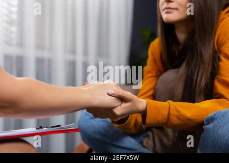 Cura, fiducia, concetto di professionalità. Primo piano di terapeuta che tiene le mani di paziente femminile, confortando il suo cliente. Sostegno ai giovani tossicodipendenti Foto Stock