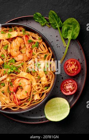 Mie Goreng in ciotola nera su piano da tavolo in ardesia scura. Cucina indonesiana tagliatelle di gamberi e verdure mescolano piatto cotto. Cibo asiatico. Vista dall'alto Foto Stock