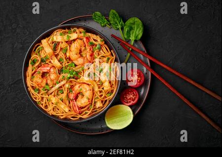 Mie Goreng in ciotola nera su piano da tavolo in ardesia scura. Cucina indonesiana tagliatelle di gamberi e verdure mescolano piatto cotto. Cibo asiatico. Vista dall'alto Foto Stock