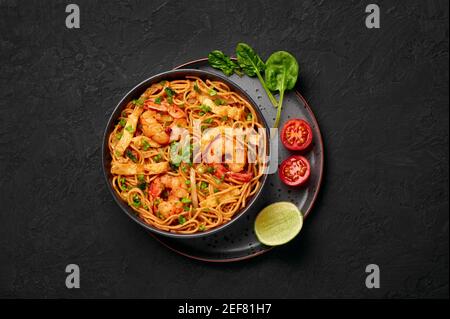 Mie Goreng in ciotola nera su piano da tavolo in ardesia scura. Cucina indonesiana tagliatelle di gamberi e verdure mescolano piatto cotto. Cibo asiatico. Vista dall'alto Foto Stock