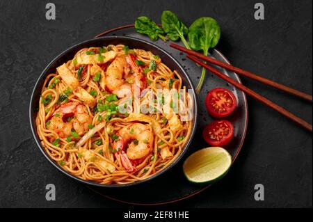 Mie Goreng in ciotola nera su piano da tavolo in ardesia scura. Cucina indonesiana tagliatelle di gamberi e verdure mescolano piatto cotto. Cibo asiatico. Foto Stock