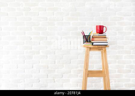 Libri, cancelleria e tazza di caffè su sgabello di legno in bianco muro di mattoni sfondo - idea, creativi e concetti di istruzione Foto Stock