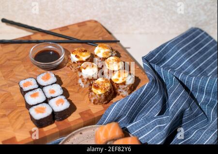 Panini di sushi giapponesi serviti su sfondo di legno. Sushi Rolls Philadelphia, rotolo caldo fritto con panna, maki, chopsticks e salsa di soia Foto Stock