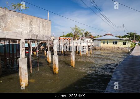 Vista sulla strada costiera del quartiere povero di Kota Kinabalu città, Malesia. Piccole case viventi, costruzioni abbandonate e passerelle su palafitte Foto Stock