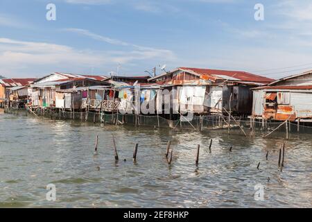 Vecchie case in legno di rickety e passerelle su palafitte. Vista costiera del povero quartiere vivente di Kota Kinabalu, Malesia Foto Stock