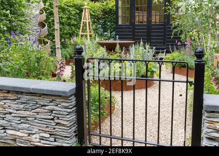 Cottage inglese giardino di campagna Un cancello di giardino in metallo nero dipinto - muro di pietra a secco con percorso di ghiaia e aiuole giardino confine Inghilterra UK Foto Stock