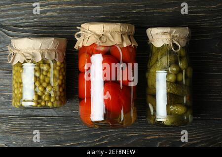 Vasetti con pomodori, cetrioli e piselli sottaceto su sfondo ligneo Foto Stock